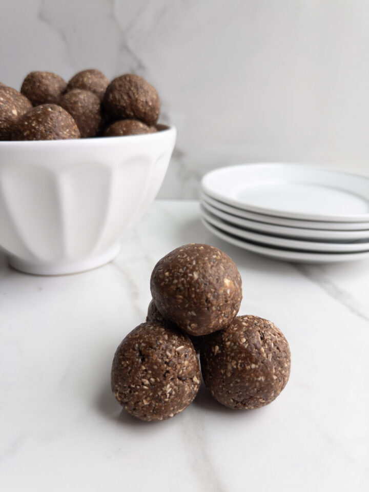 Chocolatey power balls on counter and in bowl with plates in the background