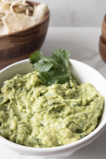 Bowl of creamy guacamole dip with chip, bowls and limes in the background