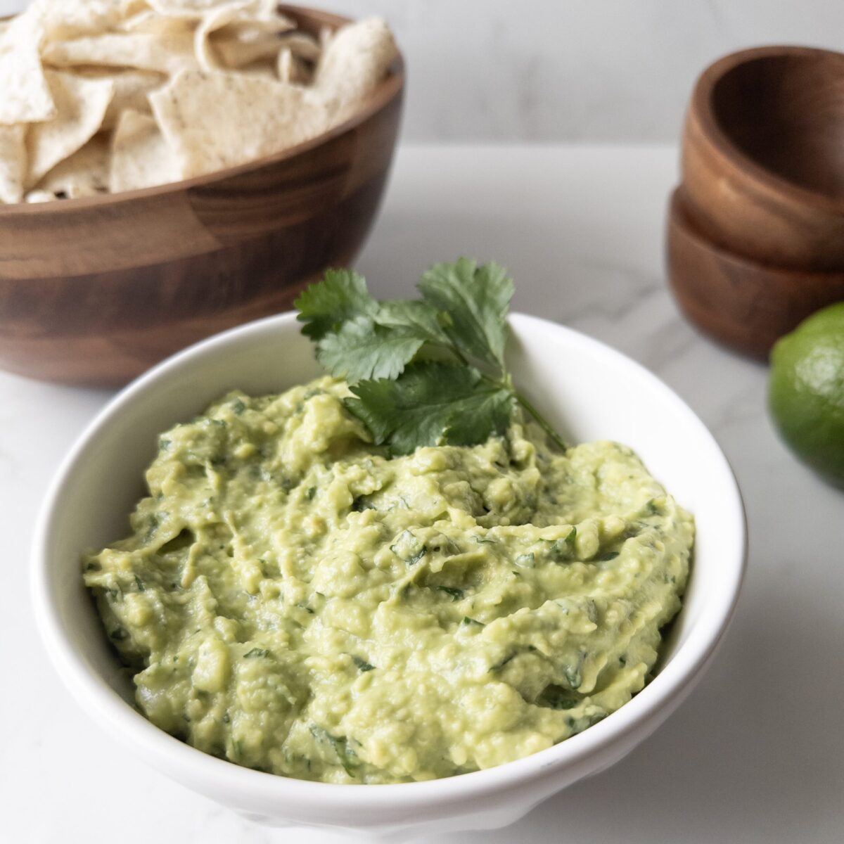 Bowl of creamy guacamole dip with chip, bowls and limes in the background