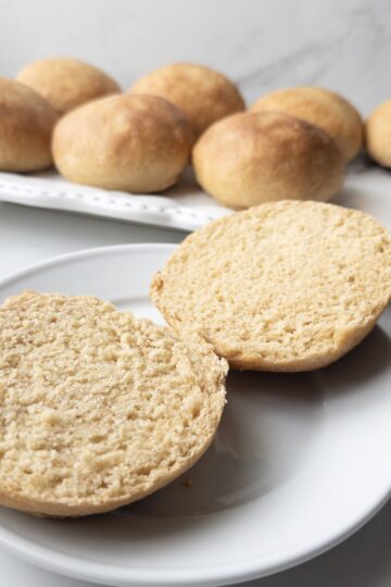 Fresh Milled Hamburger Buns sitting on a plate with a serving dish of buns in the background