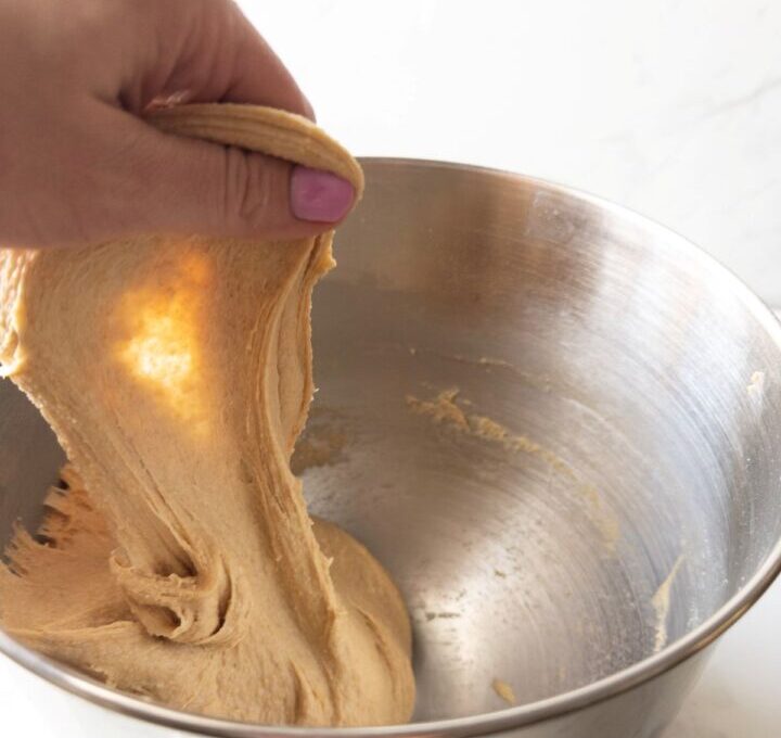 Hand pulling dough out of mixing bowl to show windowpane test
