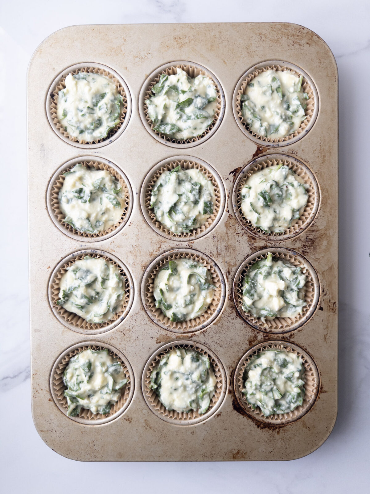 Muffin tin with paper liners filled with Savory Gluten-Free Spinach Feta Muffins wet mixture