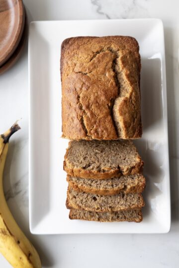 Sliced Wholesome Banana Bread on a plate with a banana, dishes & butterdish