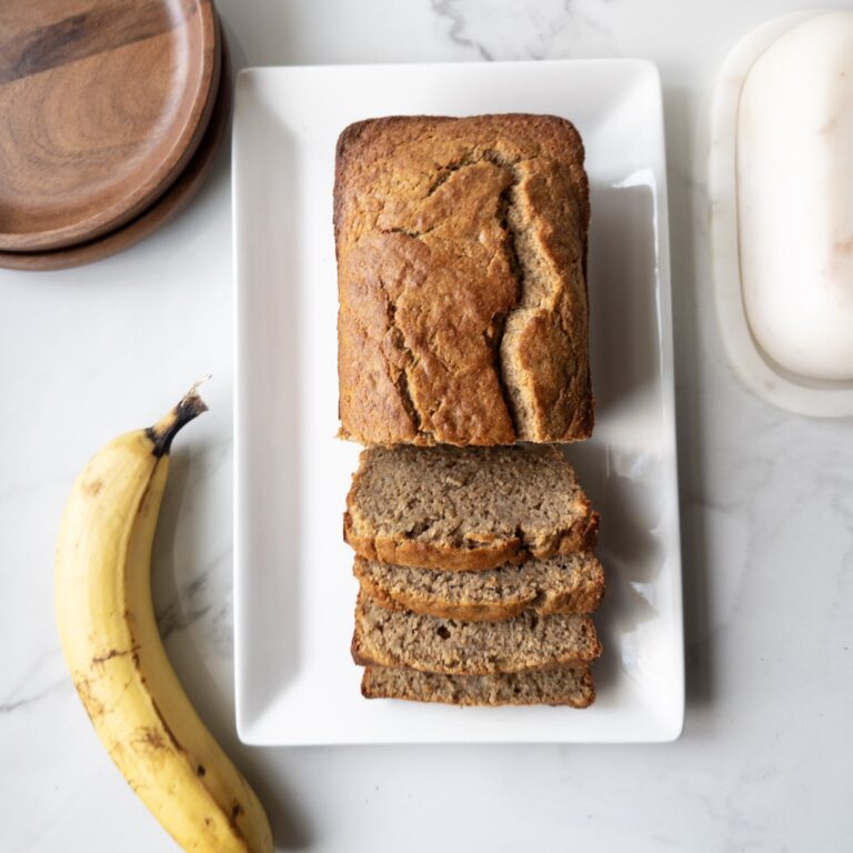 Sliced Wholesome Banana Bread on a plate with a banana, dishes & butterdish