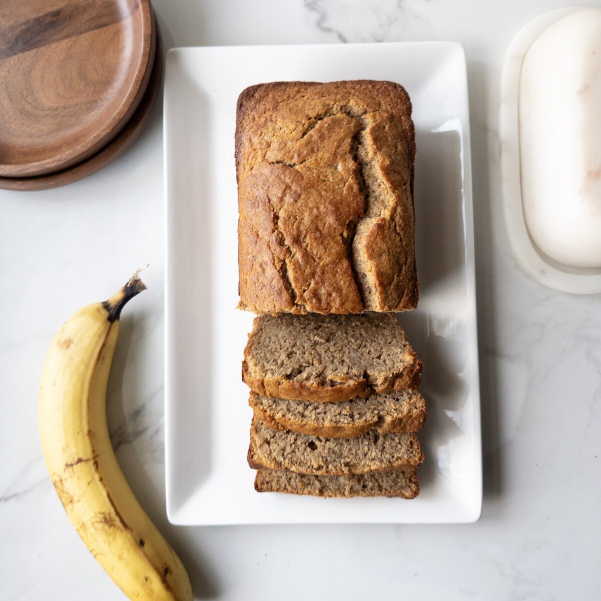 Sliced Wholesome Banana Bread on a plate with a banana, dishes & butterdish