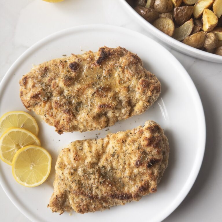 2 pieces of Gluten-Free Chicken Piccata on a plate with lemon slices and roasted potatoes in the background