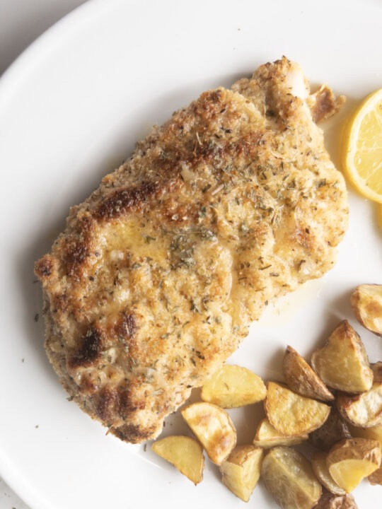 Piece of Gluten-Free Chicken Piccata sitting on a plate with a lemon slice and roasted potatoes