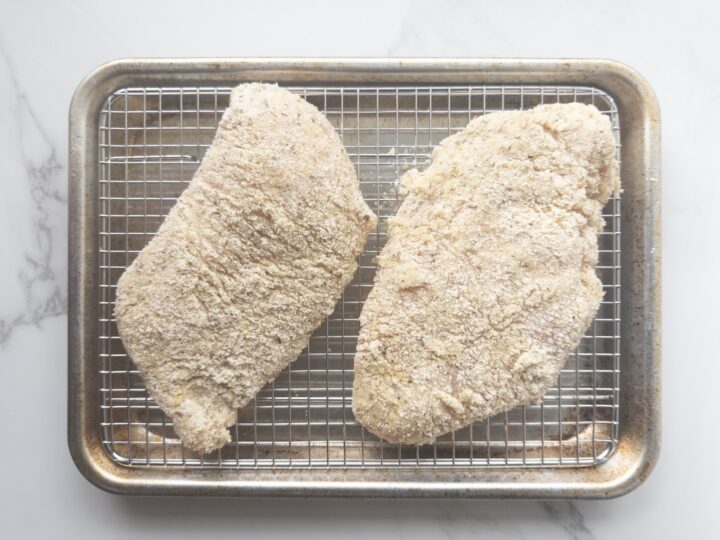 2 uncooked pieces of breaded chicken sitting on a wire lined baking sheet