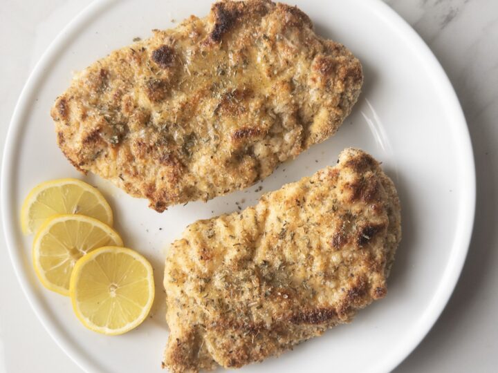 2 finished pieces of gluten-free chicken piccata sitting on a plate with lemon slices