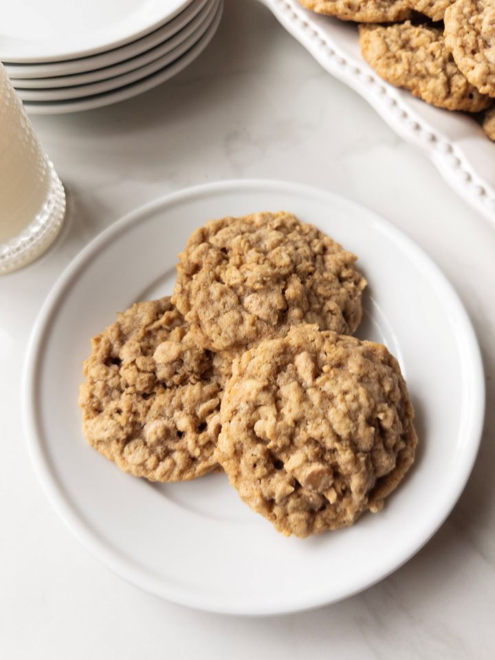 Plate of 3 Soft & Chewy Oatmeal Butterscotch Cookies with Fresh Milled Flour with milk, plates & cookies in the background