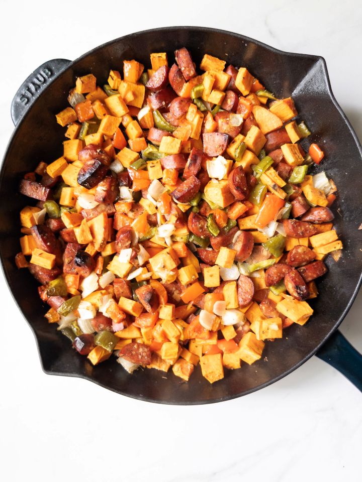 Skillet with chopped sweet potatoes, onions, bell peppers, chicken sausage, oregano, salt, and pepper after being roasted