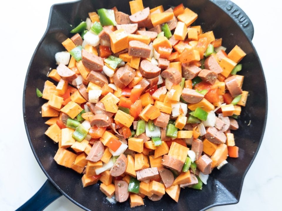 Step 2: Skillet with chopped sweet potatoes, onions, bell peppers, chicken sausage, oregano, salt, and pepper