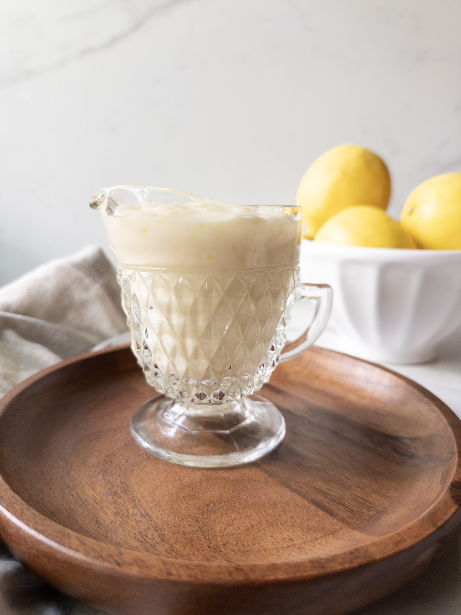 Lemon icing in a glass creamer pitcher with fresh lemons in the background