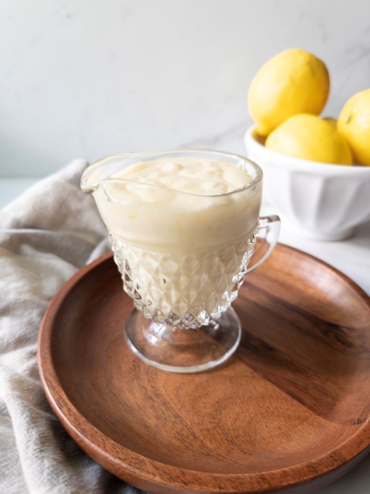 Glossy lemon icing in a glass creamer next to a bowl of lemons