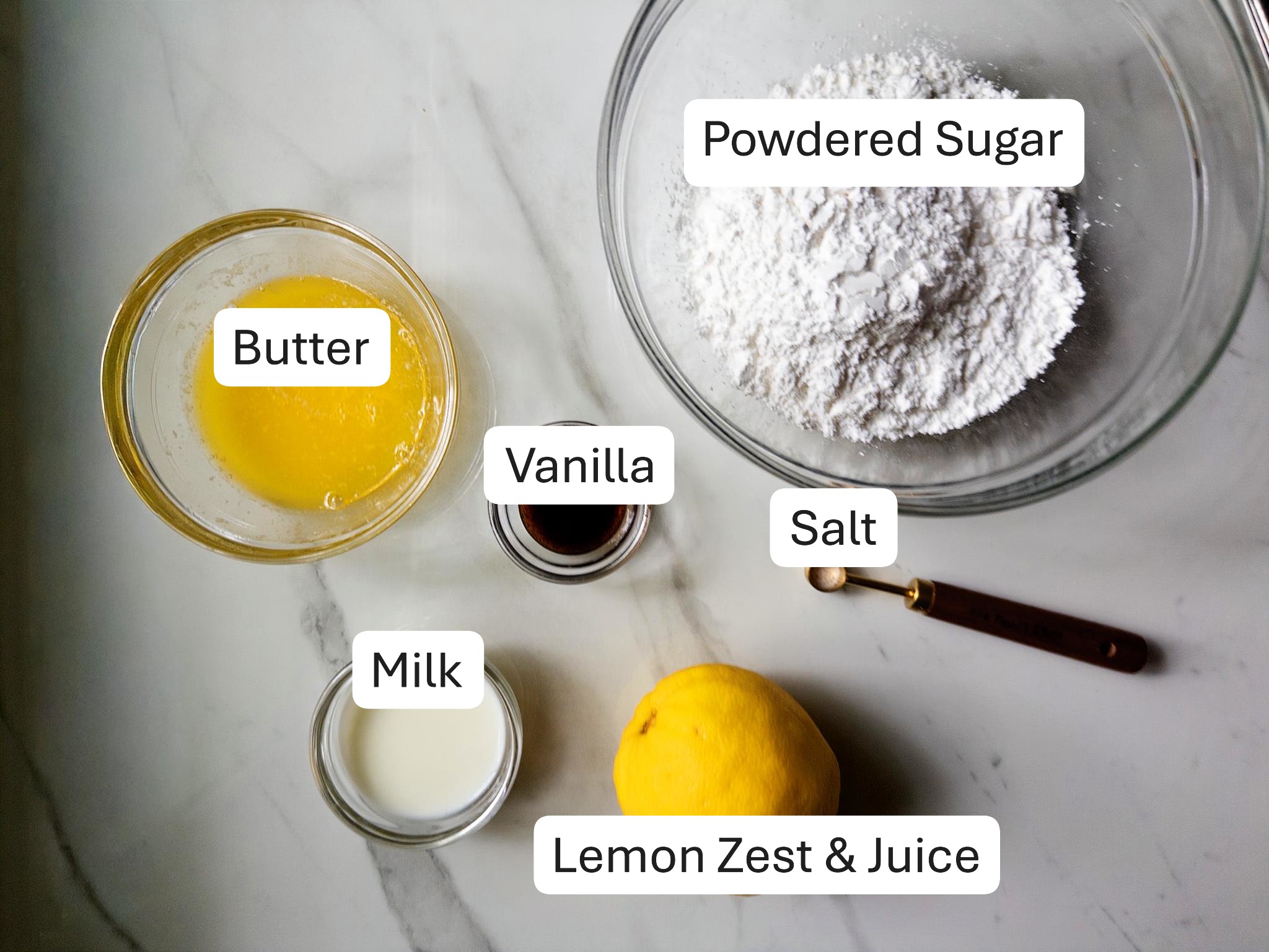 Labeled ingredients for lemon icing, including butter, powdered sugar, milk, vanilla, salt, and lemon
