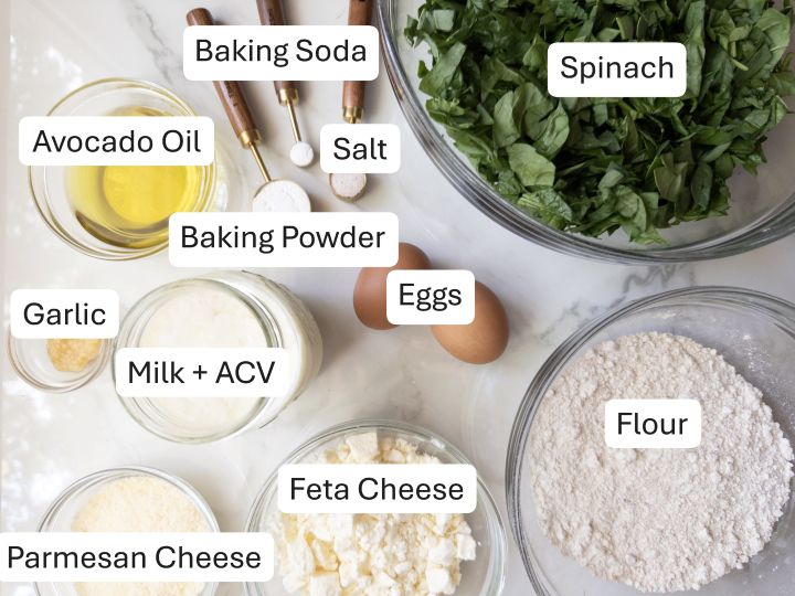 Ingredients for spinach and feta muffins with fresh milled flour, including spinach, feta, Parmesan, milk and vinegar, and flour, labeled in bowls