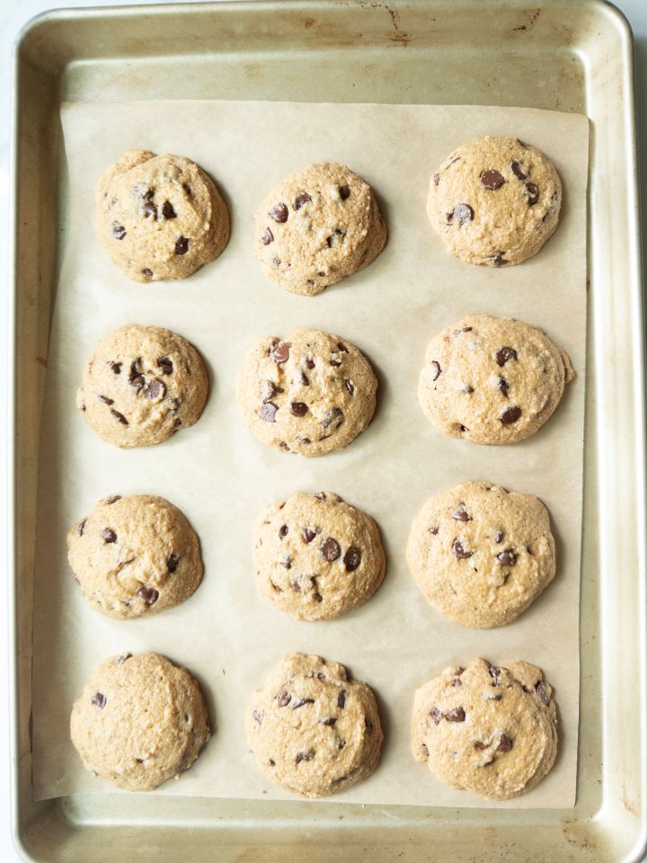 Baked naturally sweetened chocolate chip cookies on a parchment-lined baking sheet, fresh out of the oven with set edges.