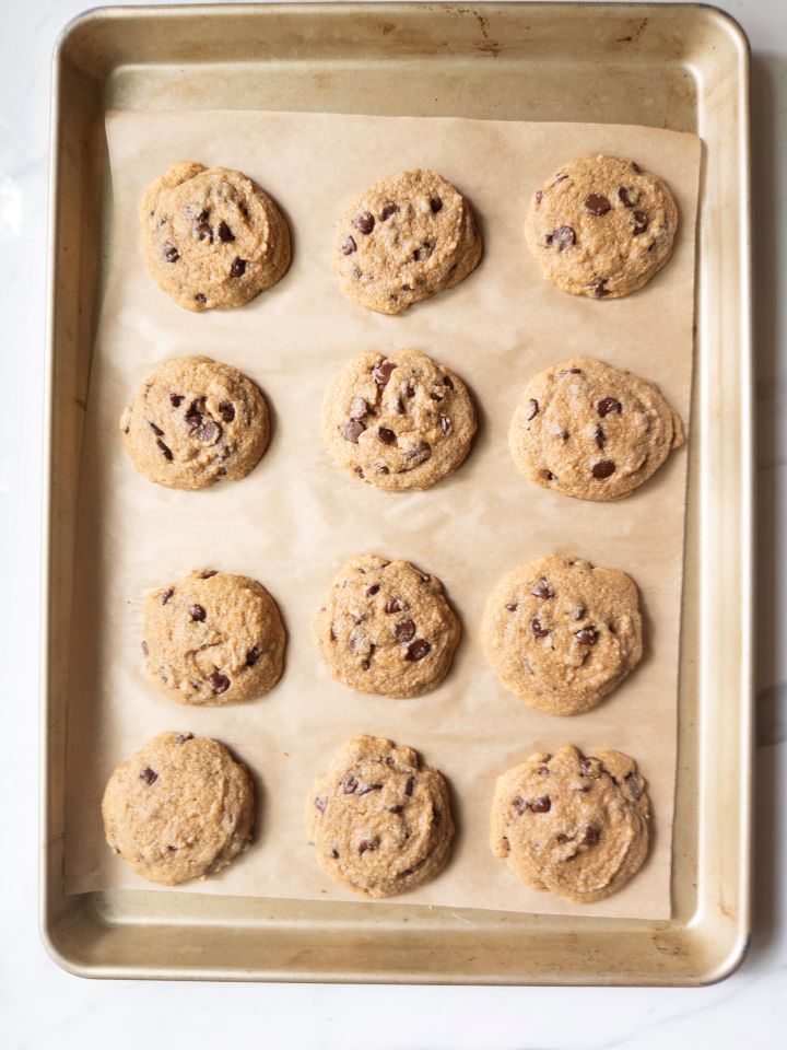Naturally sweetened chocolate chip cookies resting on a baking sheet after baking, before being moved to a cooling rack.