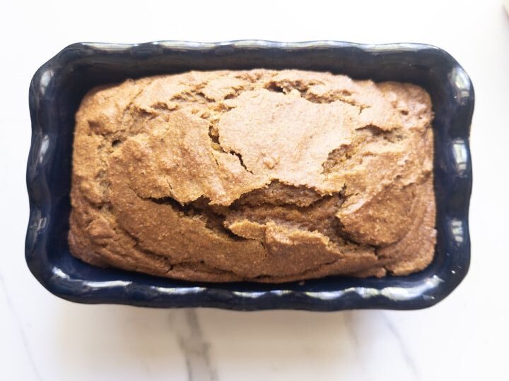 Freshly baked pumpkin bread loaf with a cracked golden-brown top, cooling in the loaf pan