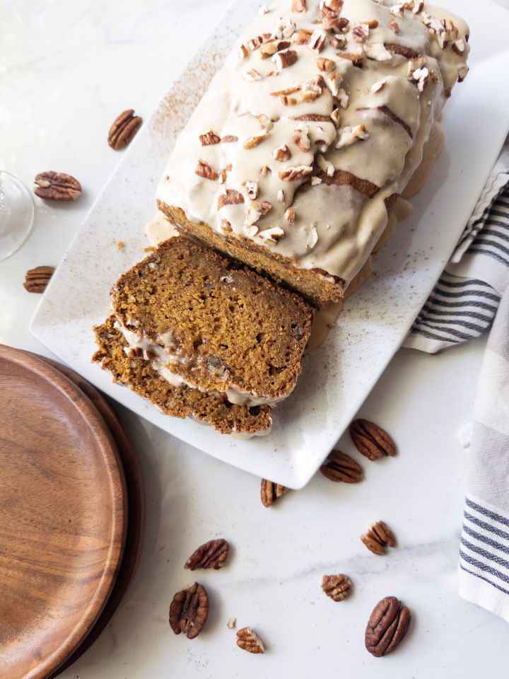 Slices of pumpkin bread drizzled with maple icing, served on a plate scattered with pecans