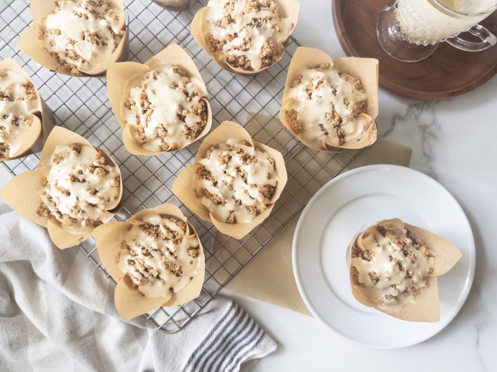 Pumpkin muffins topped with crumbly streusel and drizzled with maple icing, cooling on a wire rack next to a glass of milk.