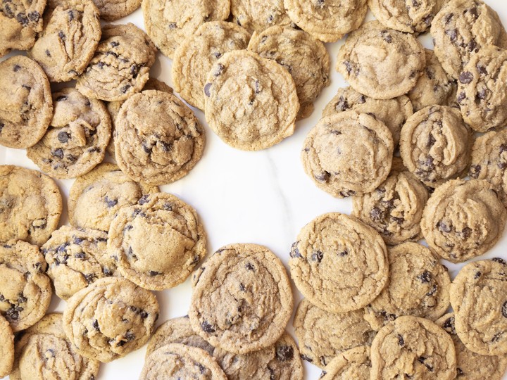 Overhead view of a large batch of fresh milled flour chocolate chip cookies scattered on a white marble surface