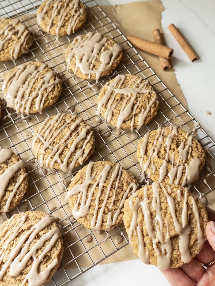 Chewy pumpkin cookies drizzled with brown butter icing, cooling on a wire rack with one cookie being held.