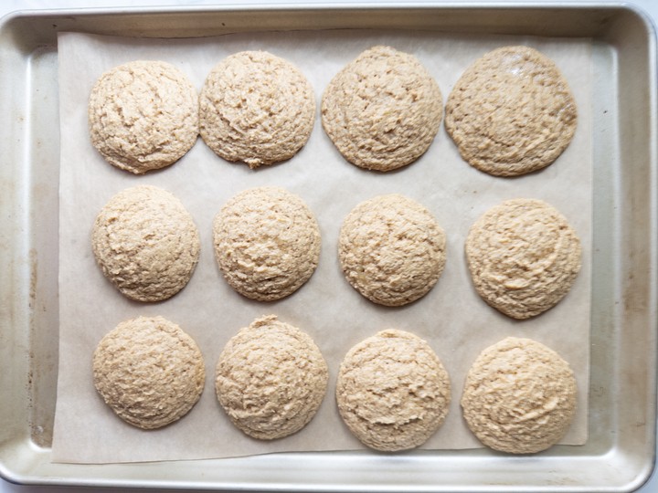 A dozen baked pumpkin cookies, puffed with set edges, on a parchment-lined baking sheet.