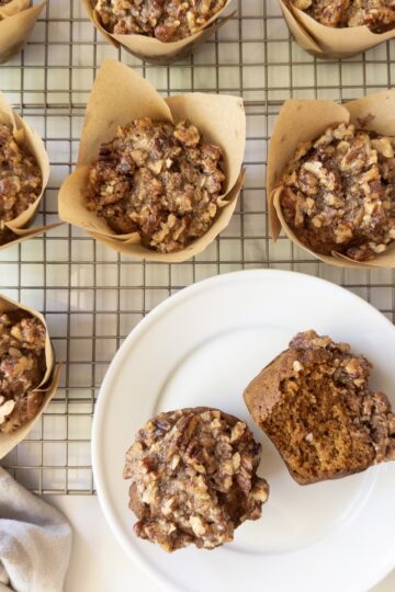 Pumpkin muffins with a maple pecan crunch topping on a wire rack, with one plated and split open to show the moist crumb.