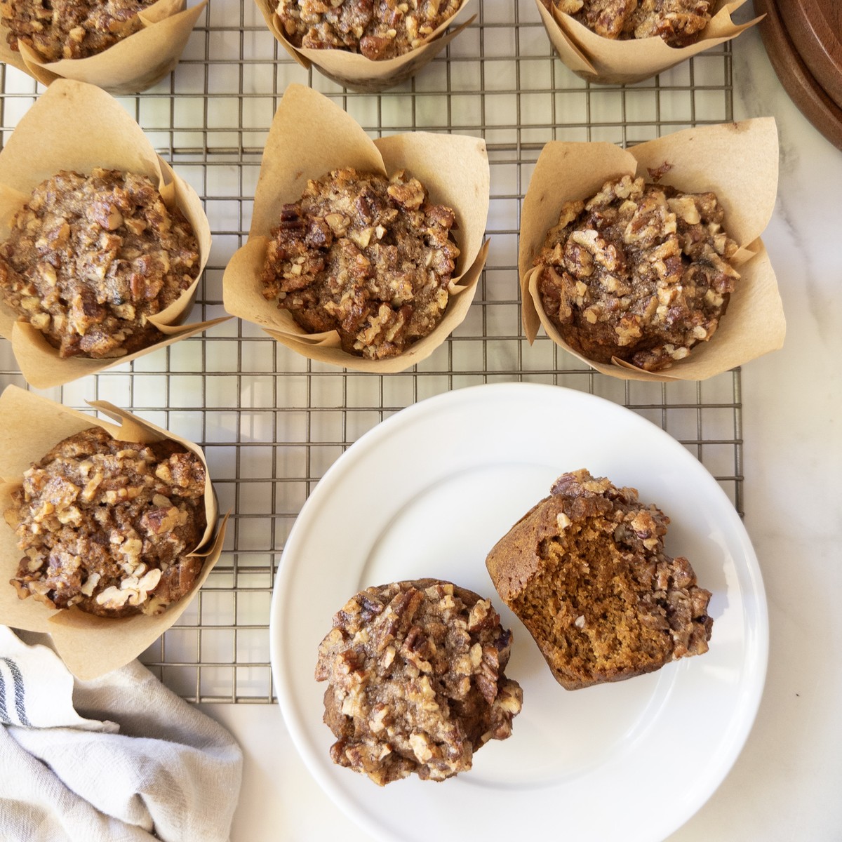 Pumpkin muffins with a maple pecan crunch topping on a wire rack, with one plated and split open to show the moist crumb.