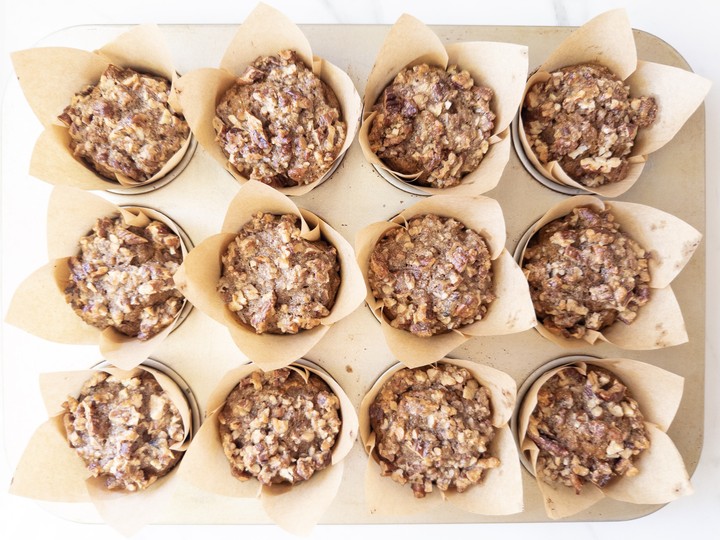 Freshly baked pumpkin muffins in the tin with a glossy, golden pecan topping.