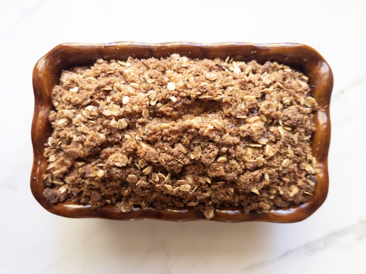 Baked apple crisp bread in a brown loaf pan with a golden oat crumb topping.