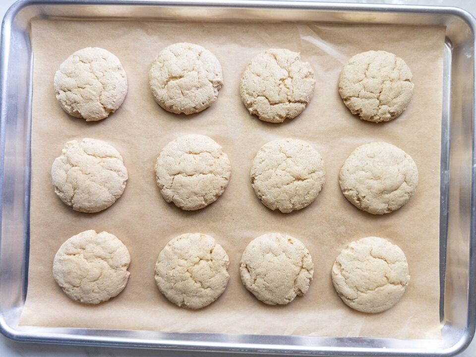 Twelve baked soft sugar cookies with lightly crackled tops on a parchment-lined cookie sheet.