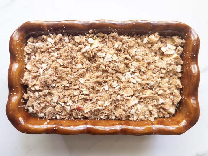 Unbaked apple crisp bread in a brown loaf pan covered with an oat crumb topping.