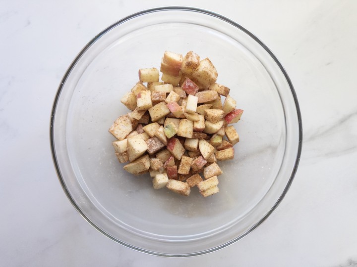 Small diced apples tossed with cinnamon and flour in a glass bowl.